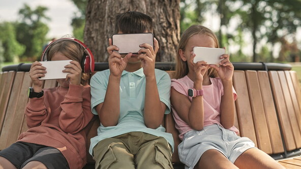 stock-photo-obscure-faces-of-children-using-and-watching-smartphones-on-wooden-bench-in-park-outdoors-boys-and-2166385651.jpg